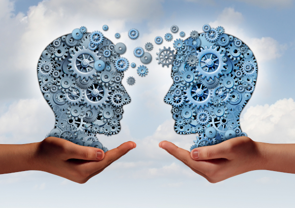 Business technology concept as two hands holding a group of machine gears shaped as a human head as a symbol and metaphor for the transfer of industry information or corporate training.